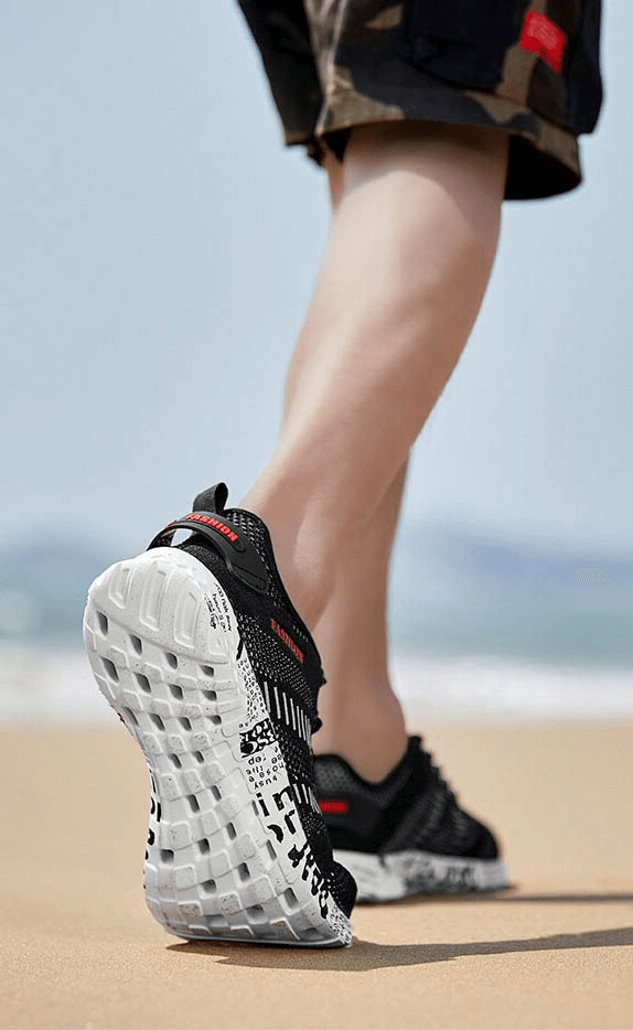 Man wearing Men's Casual Lace-up Mesh Sneakers walking on beach, showcasing soft outsole and geometric pattern for comfort and style.