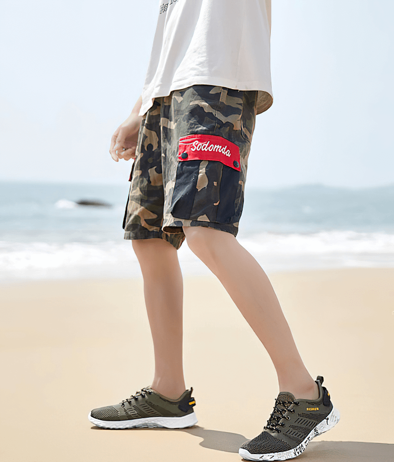 Person wearing men's casual lace-up mesh sneakers and camo shorts on a beach