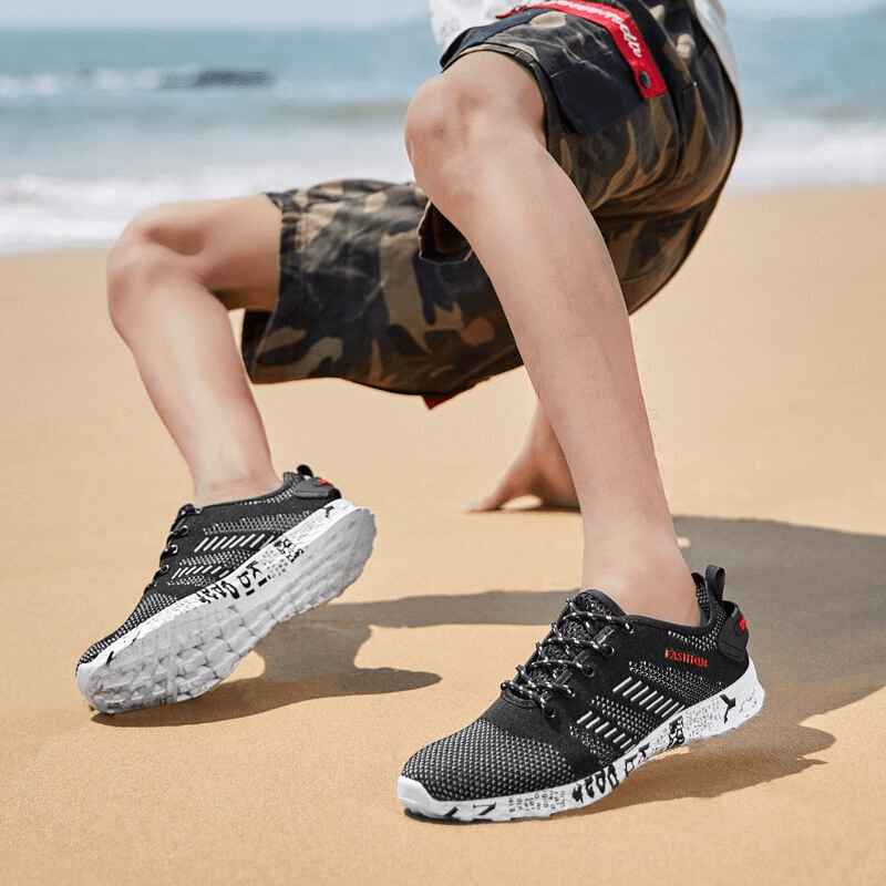 Man wearing men's casual lace-up mesh sneakers SF0805, black with white sole, running on a sandy beach.