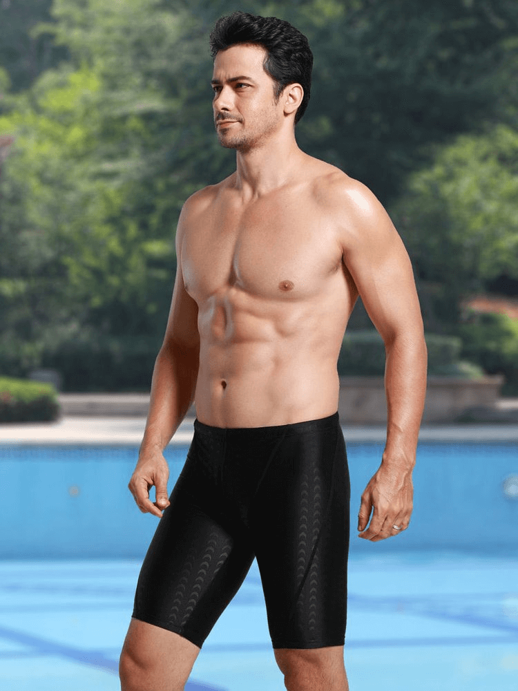 Male model wearing black quick-dry swim shorts by the pool, showcasing an elastic waist and comfortable fit ideal for swimming.