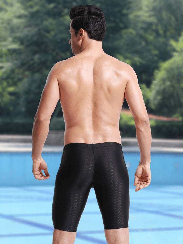 Man wearing black swimming shorts by a pool, showcasing elastic, quick-dry, waterproof fit. Perfect for water sports and outdoor fun.