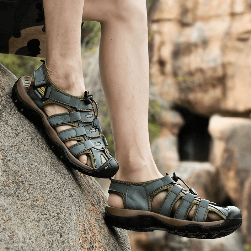 Men's leather outdoor beach sandals on rocky terrain, showing comfort and durability with elastic straps and rubber soles.