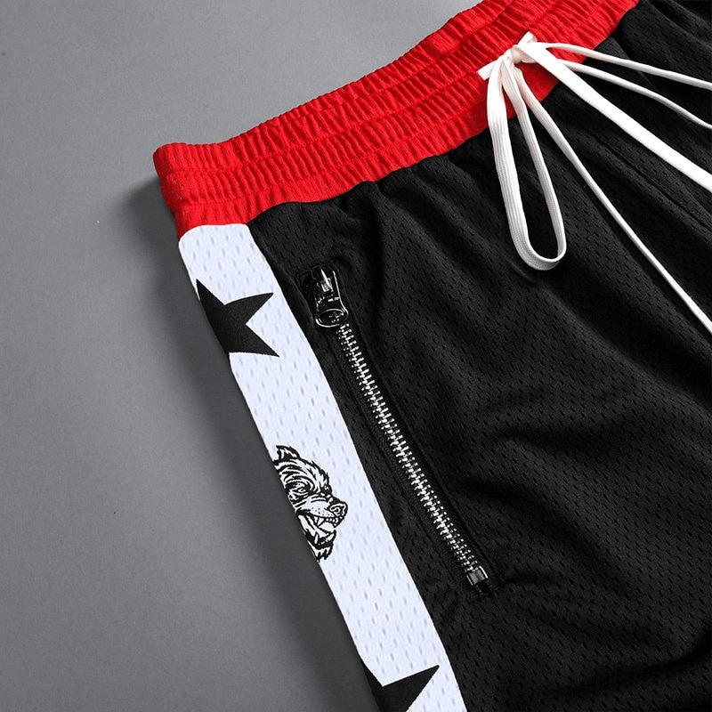 Close-up of men's black basketball shorts with red waistband, featuring a side zipper pocket and star pattern on white panel.