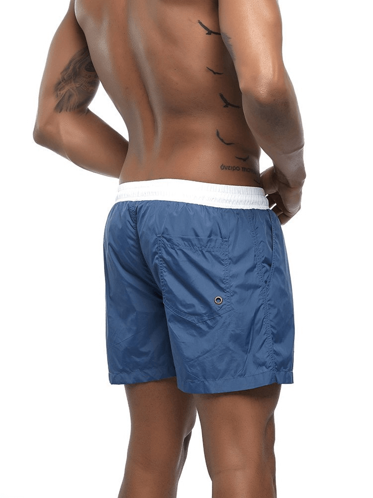 Back view of a man wearing blue quick dry swimming shorts, ideal beachwear for men, featuring a solid design and comfortable fit.