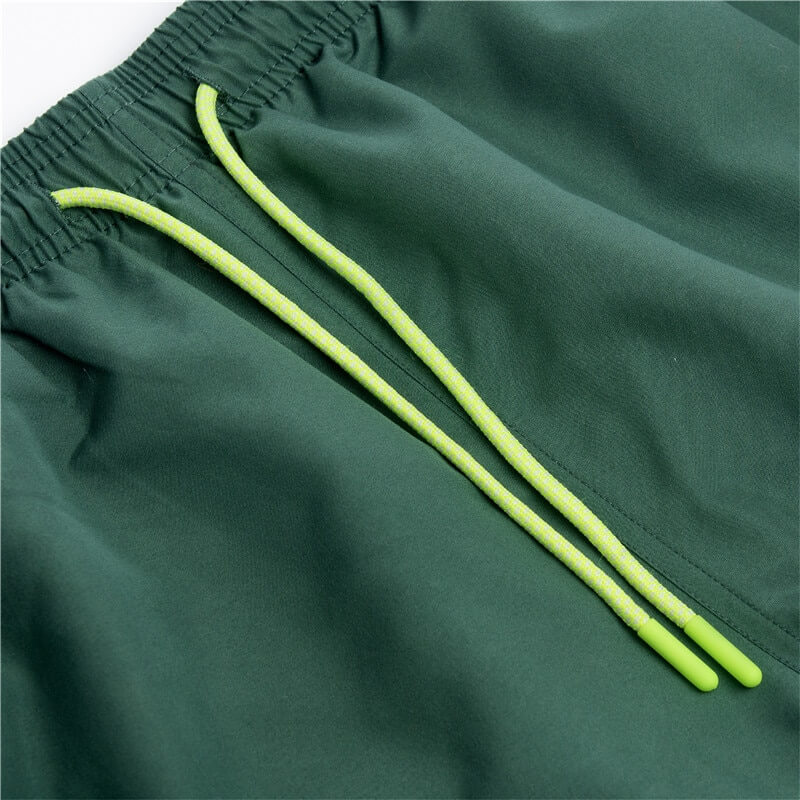 Close-up of men's green solid color boardshorts with yellow drawstrings and pockets, made from quick-drying polyester.