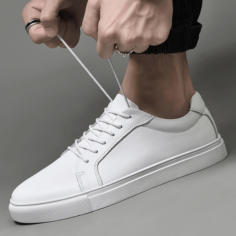 Person tying white men's leather sports sneakers with flexible flat sole, SF1177 model, featuring lace-up closure for secure fit.