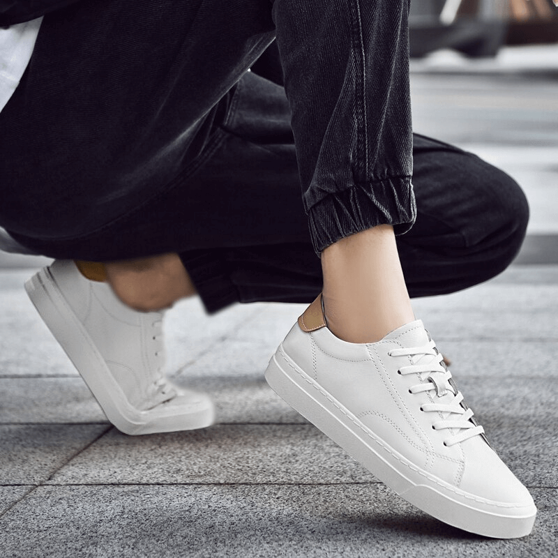 Men's sporty flexible flat sole sneakers in white leather, worn casually on the street with black pants, showcasing comfort and style.