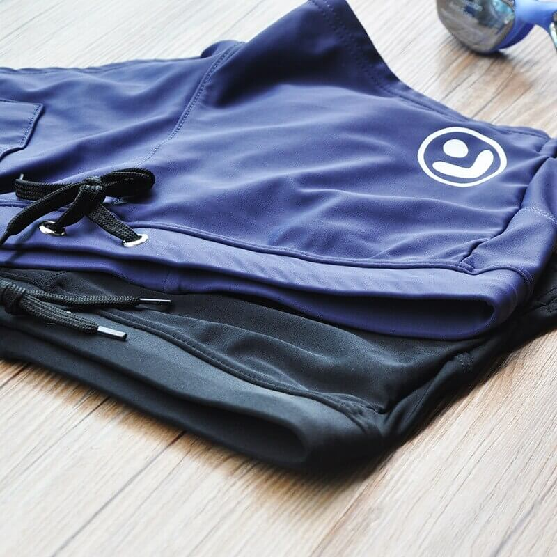 Men's swim trunks with zipper pocket in navy and black, lightweight quick-dry polyester for comfort and style, on wooden surface.