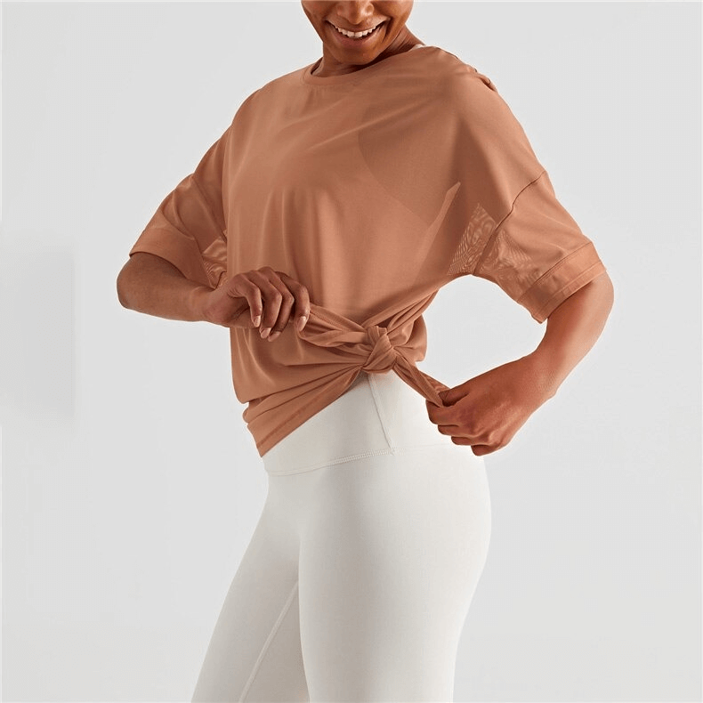 Woman in a mesh casual sports T-shirt tying a knot, showcasing short sleeves and quick-drying fabric ideal for fitness enthusiasts.