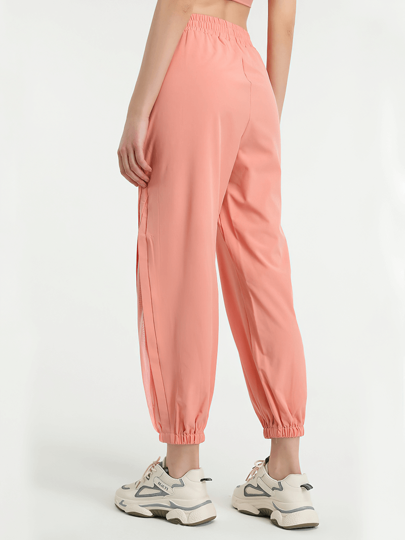 Woman wearing coral mesh drawstring running trousers ideal for workouts, yoga, and sports; ankle-length with an elastic waistband.