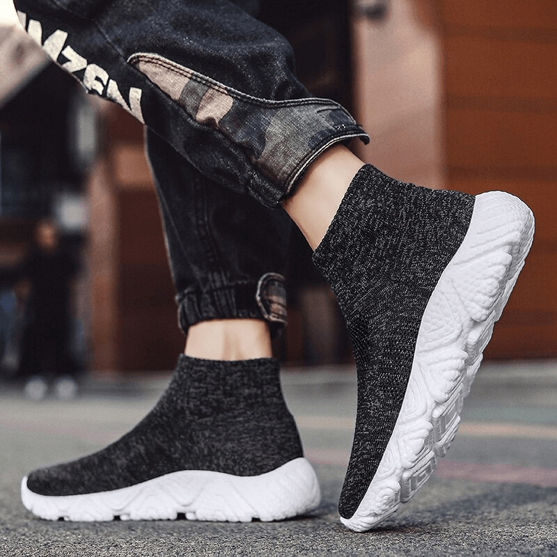 Person wearing black mesh elastic breathable unisex sneakers with a white sole on a street, highlighting the slip-on design and style.