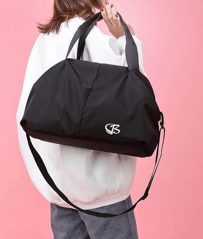 Woman carrying a stylish black multifunction waterproof large capacity gym bag against a pink background, perfect for fitness enthusiasts.