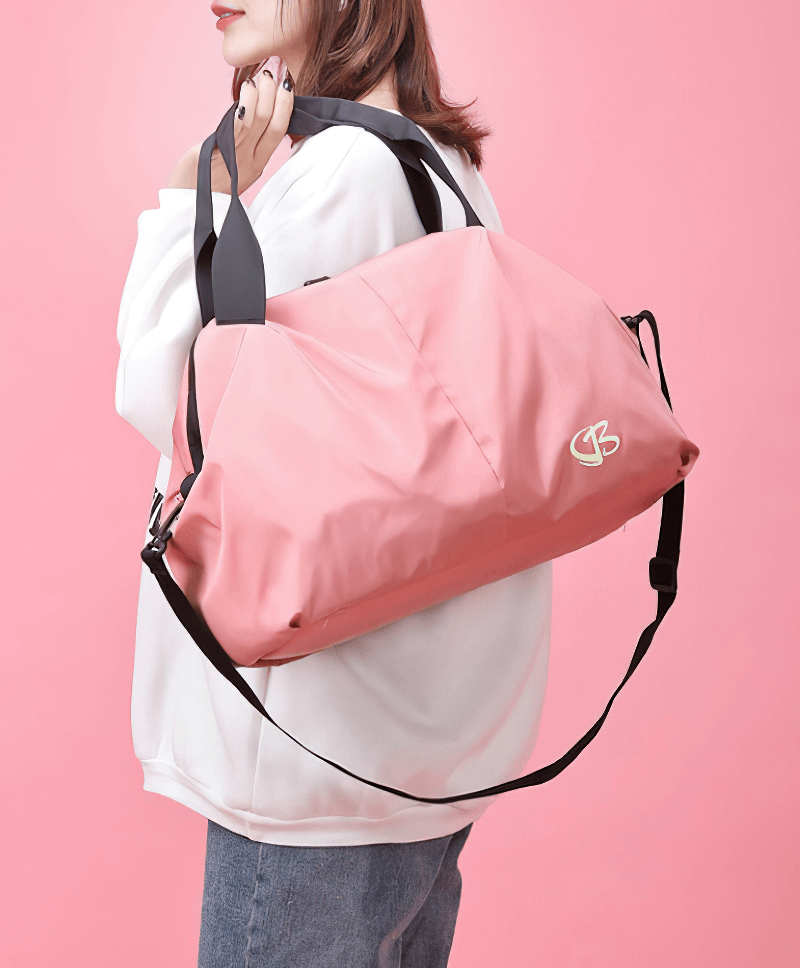 Pink multifunction waterproof women's gym bag with black straps worn over the shoulder against a pink background
