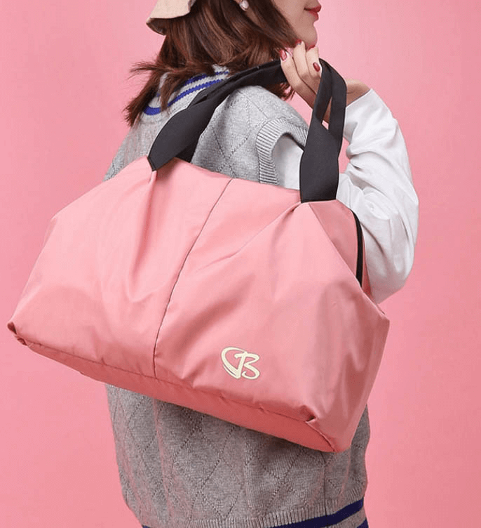 Woman carrying a pink, waterproof, large capacity gym bag with black straps, perfect for stylish fitness and travel needs.