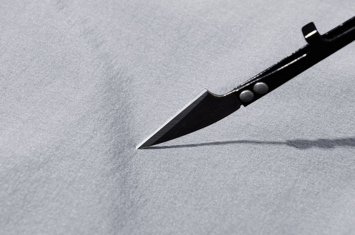 Close-up of waterproof fabric with knife demonstrating durability of hiking trousers for men.