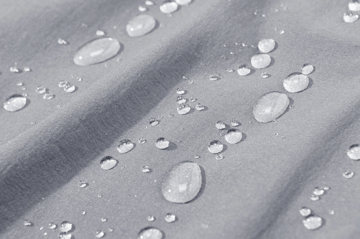 Water droplets on gray waterproof fabric of men's hiking pants, showing its water-resistant capability.