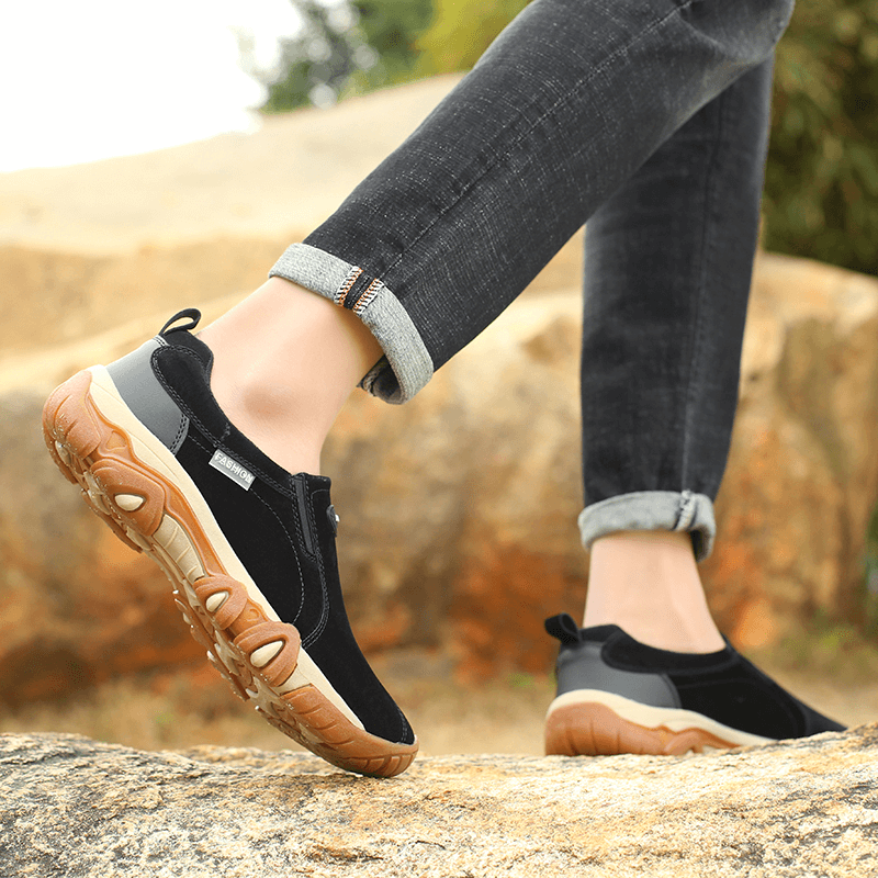 Man wearing non-slip outdoor hiking shoes with a rubber outsole, standing on rocks, showcasing the shoe's grip and comfort.