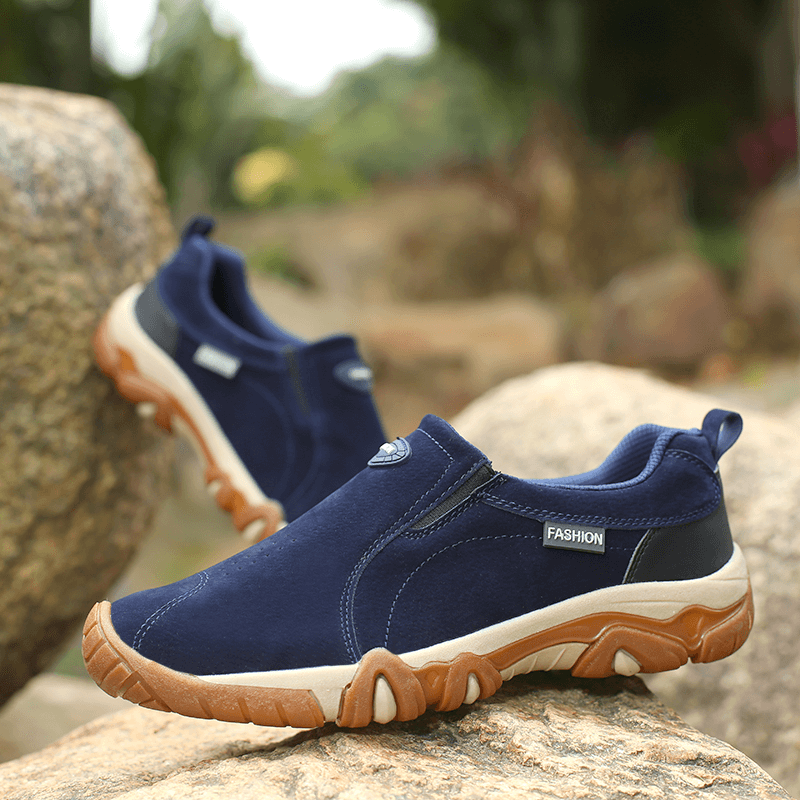 Men's blue non-slip outdoor hiking shoes with rubber outsole on rocky terrain.