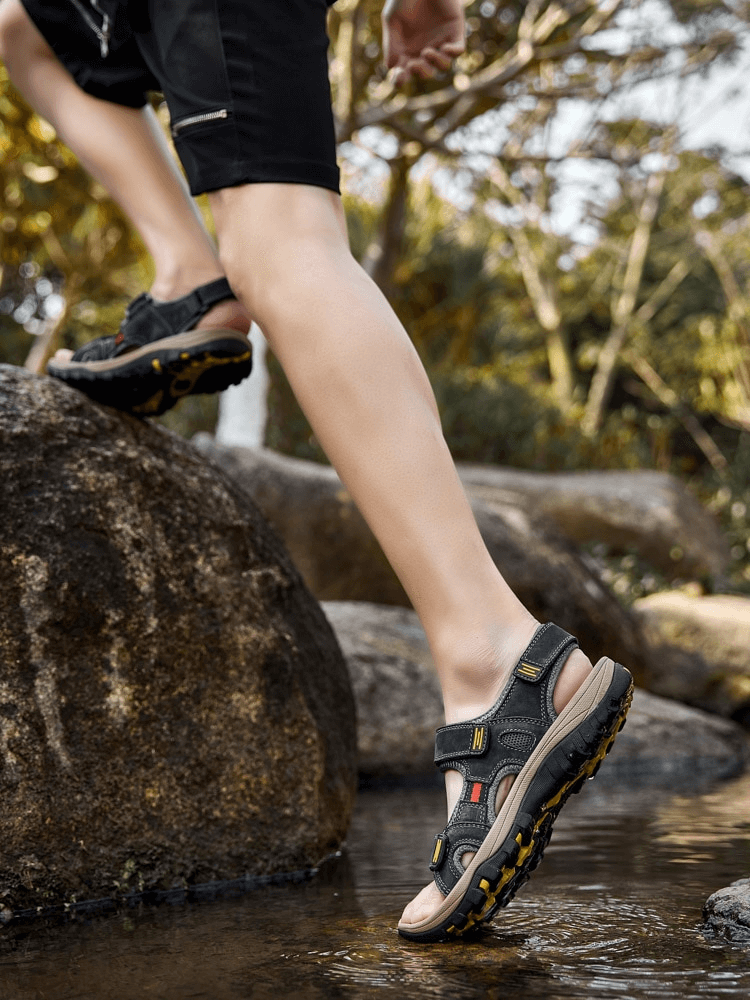 Man wearing open toe tactical leather sandals with adjustable Velcro, navigating through nature, showcasing comfortable outdoor style.