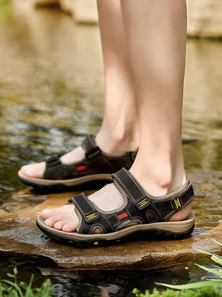 Open Toe Tactical Leather Men's Sandals with Adjustable Velcro on a rock by water, featuring solid pattern and flat heel.