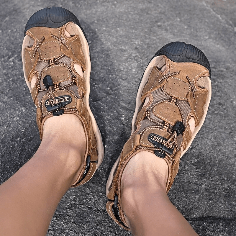 Person wearing brown leather tactical trekking sandals on a rocky surface.