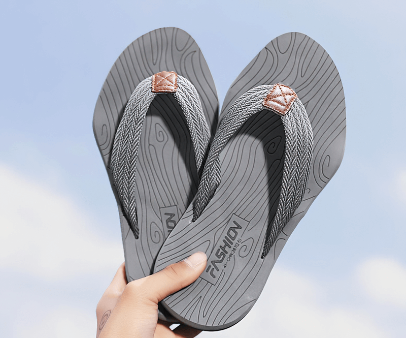 Person holding gray non-slip beach flip flops with patterned design and sturdy sole, perfect for outdoor activities.