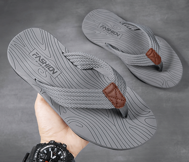 Gray non-slip beach flip flops for men with thick rubber outsoles and stylish design held in hand against a plain background.