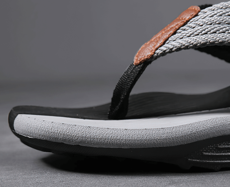Close-up of a black and gray beach flip flop with non-slip rubber sole and polyester strap, ideal for outdoor activities.