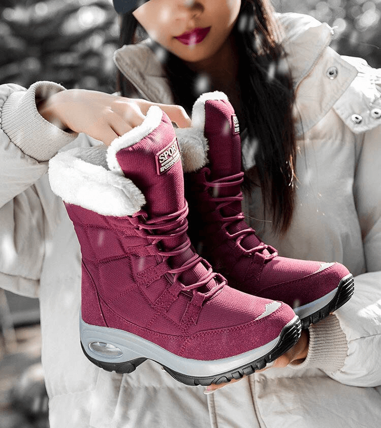 Woman holding magenta waterproof outdoor snow boots with fur lining, ideal for winter trekking, featuring durable traction soles.