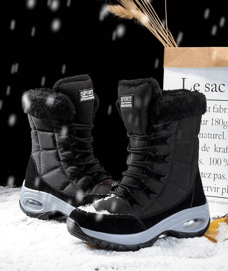 Black waterproof women's snow boots with fur lining, perfect for outdoor winter trekking, displayed on snow with decorative background.