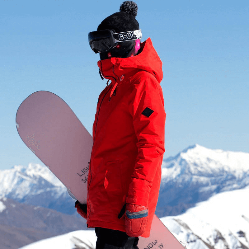 Woman wearing a red outdoor snowboarding jacket and holding a snowboard in the mountains.
