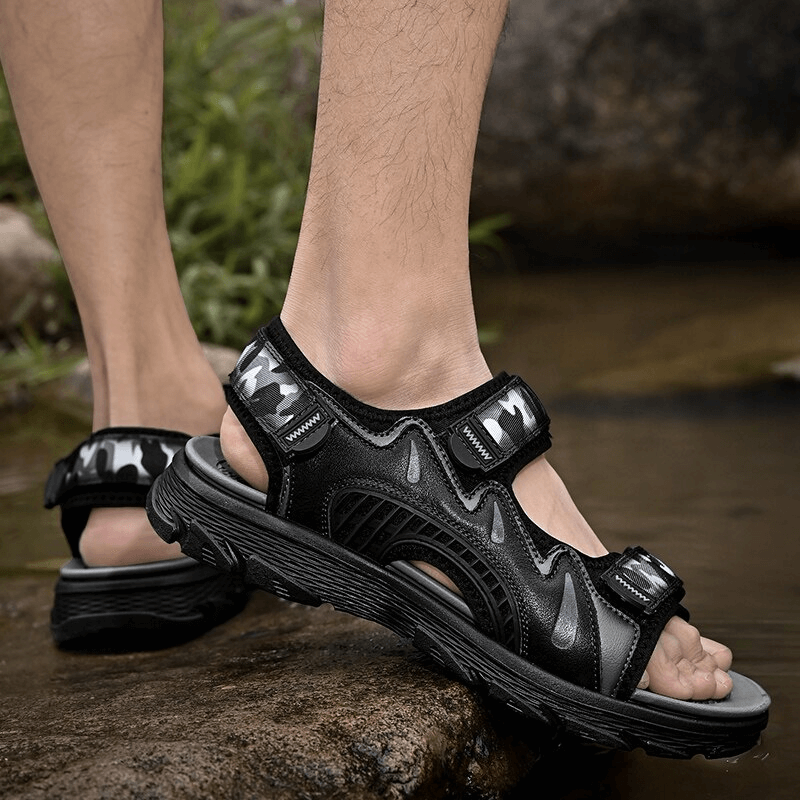 Man walking in black outdoor ultralight soft-soled sandals over rocky stream.