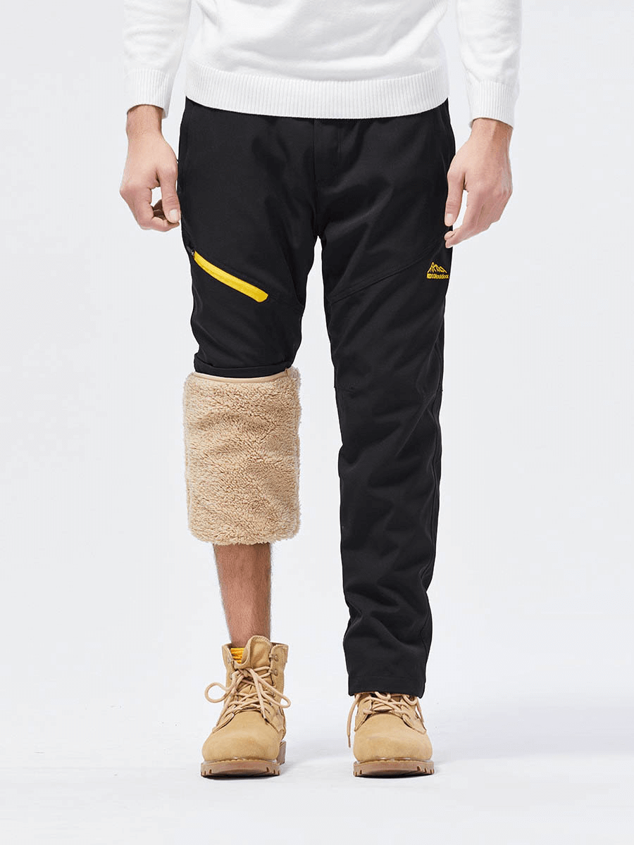 Men's outdoor windproof ski pants with removable liner, black with yellow accents, shown worn with boots, highlighting knee section.