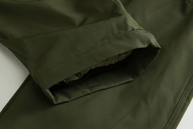 Close-up of green outdoor windproof ski pants with removable liner, highlighting durable fabric and secure zipper closure.