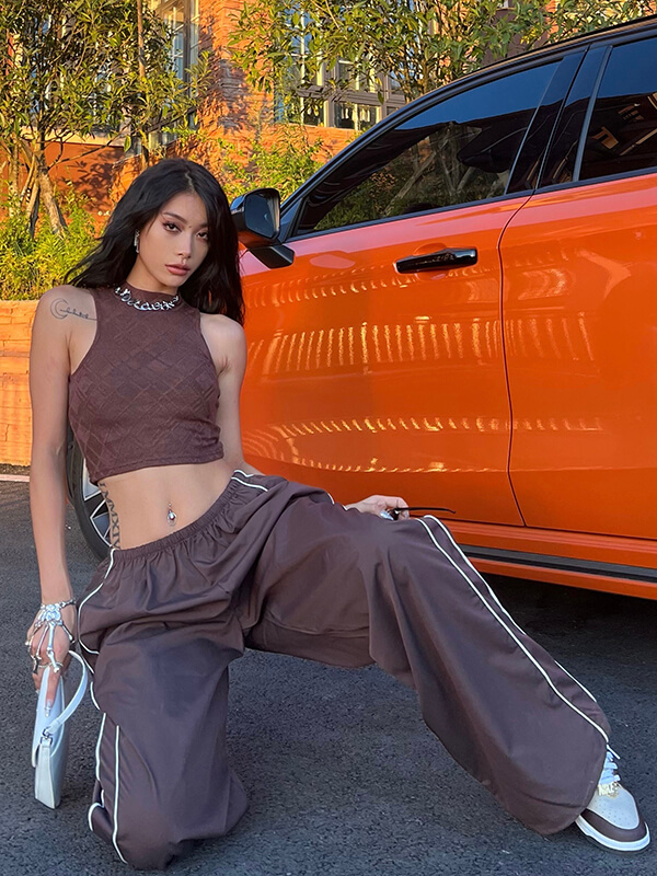 Stylish woman wearing oversized baggy high-waisted sweatpants and crop top, posing by an orange car.