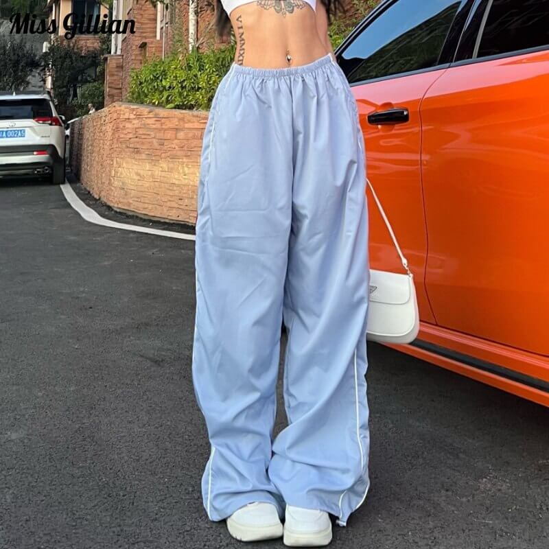 Woman wearing oversized high-waisted baggy sweatpants in light blue with side pockets, standing by an orange car.