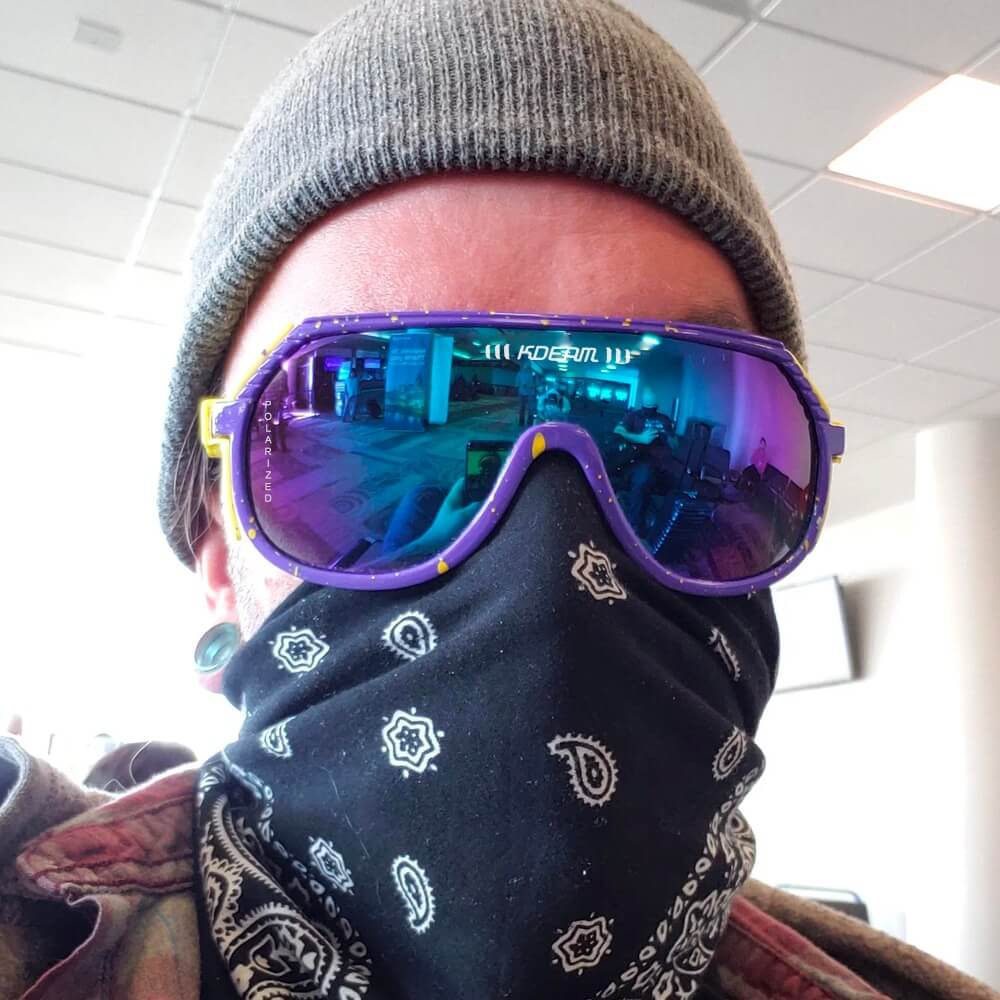 Person wearing purple reflective sports sunglasses and a beanie indoors.