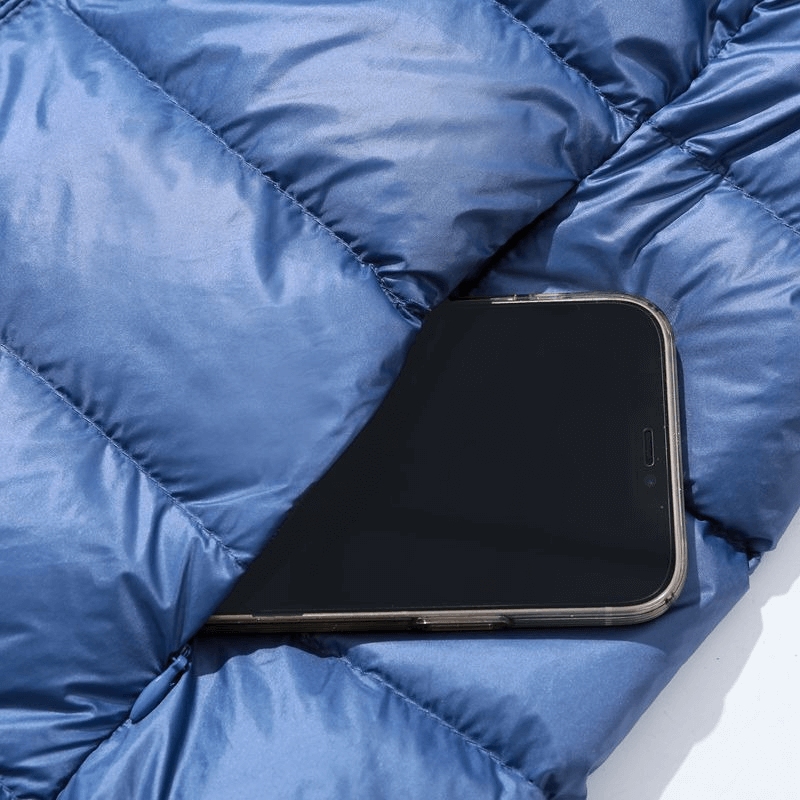 Blue puffer jacket with pocket showing a smartphone, highlighting practicality and style.