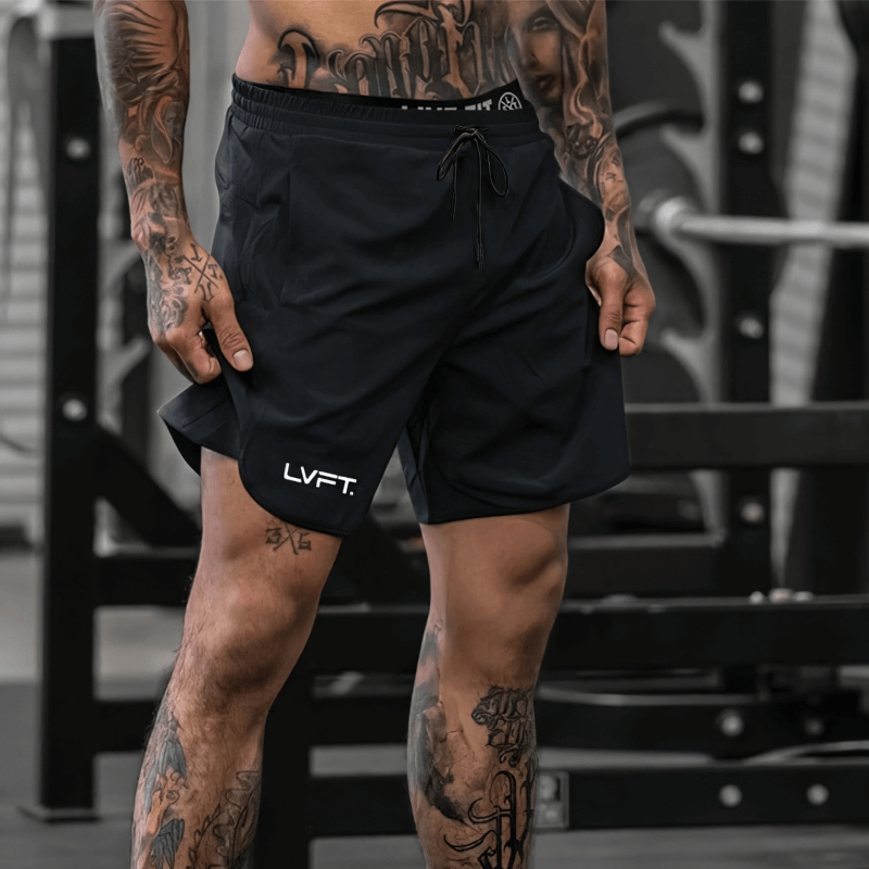 Man wearing black quick-drying sports training shorts with tattooed legs in a gym setting.