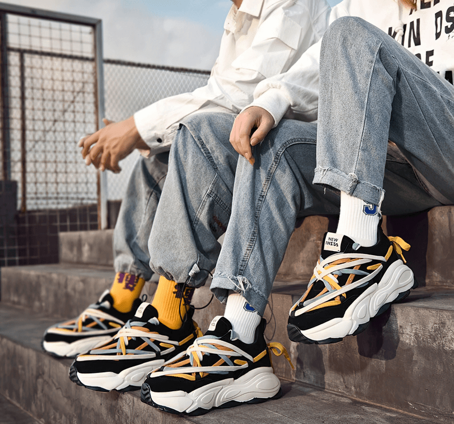 Trendy duo wearing SF0375 running sneakers with thick bottoms and colorful laces, sitting stylishly on steps in casual attire.