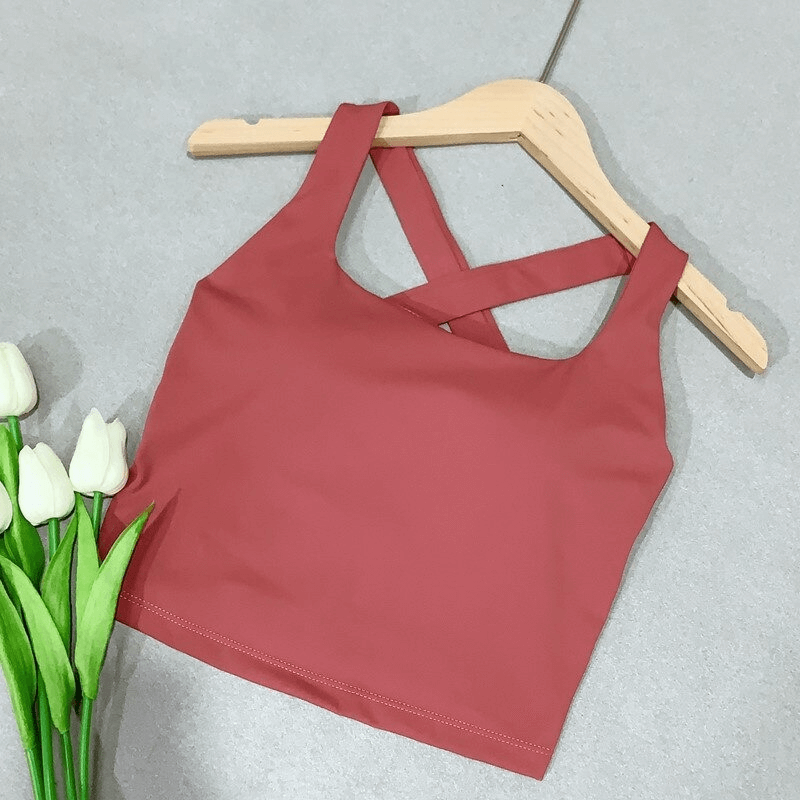 Red cross back women's running tank top for yoga and workouts, made of breathable Nylon and Spandex on a hanger next to tulips.
