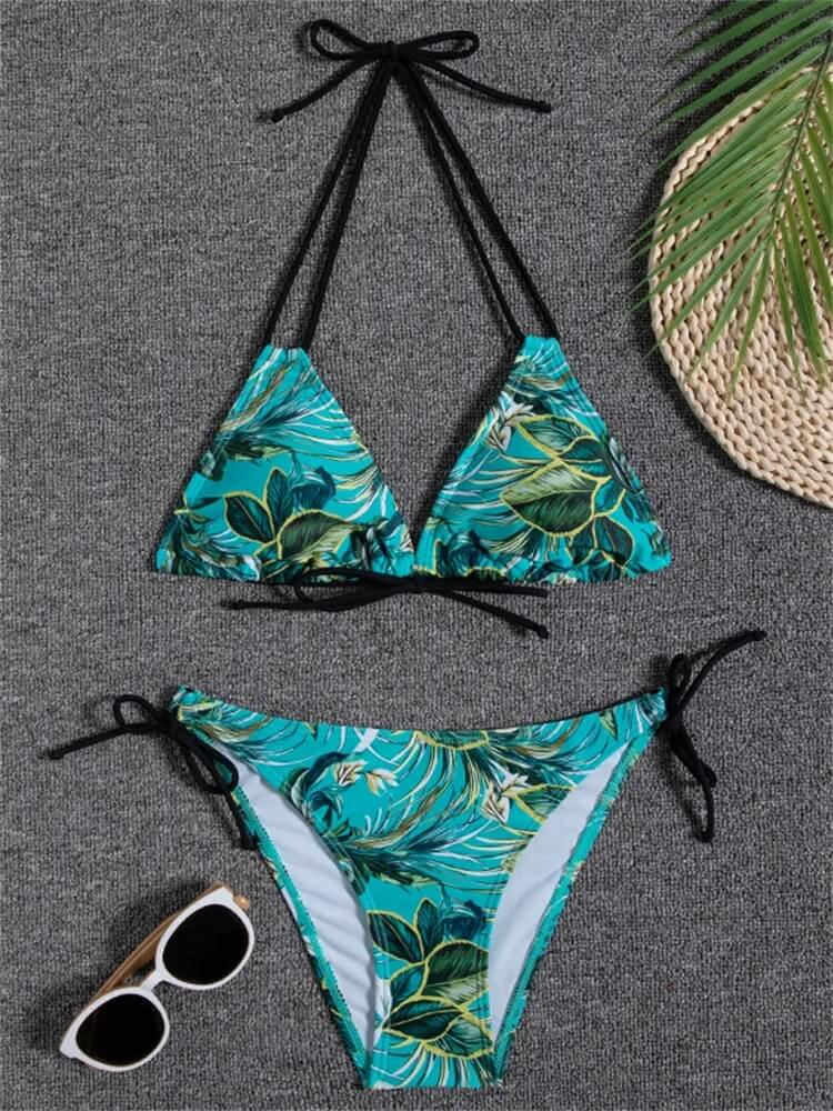 Tropical print bikini on gray background with sunglasses and palm leaf, perfect for a stylish beach day.