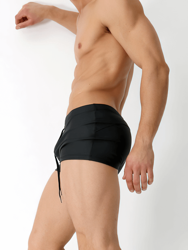 Man in black solid color drawstring swimming trunks showcasing stylish and flexible beachwear made from spandex and nylon.