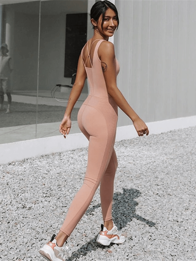 Woman wearing a peach fitness jumpsuit for yoga, showing style and comfort during outdoor exercise.