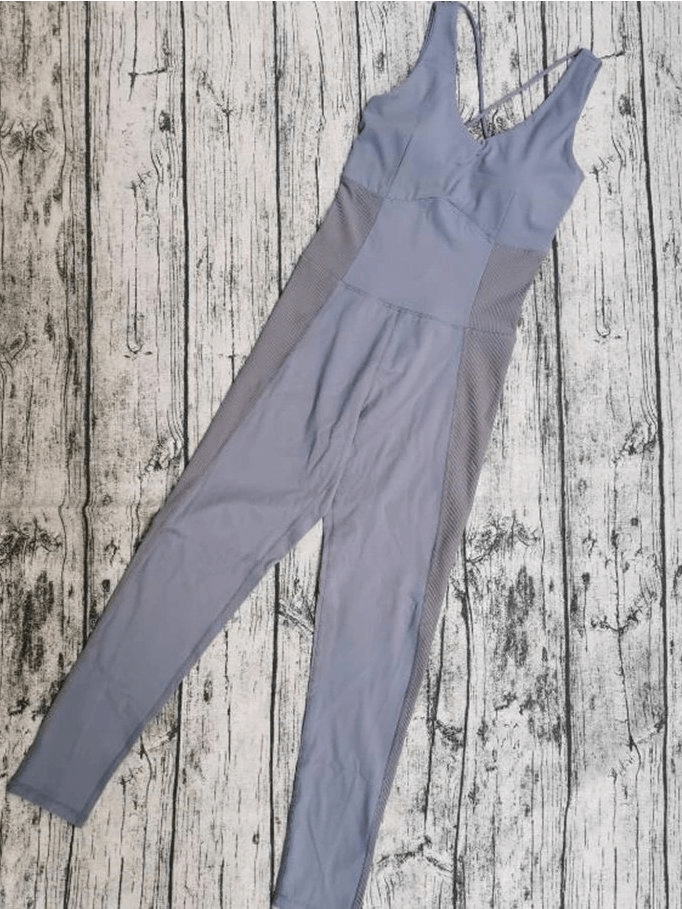 Stylish women's elastic fitness jumpsuit for yoga or sports, in breathable fabric, solid color and one-piece design on wooden backdrop.