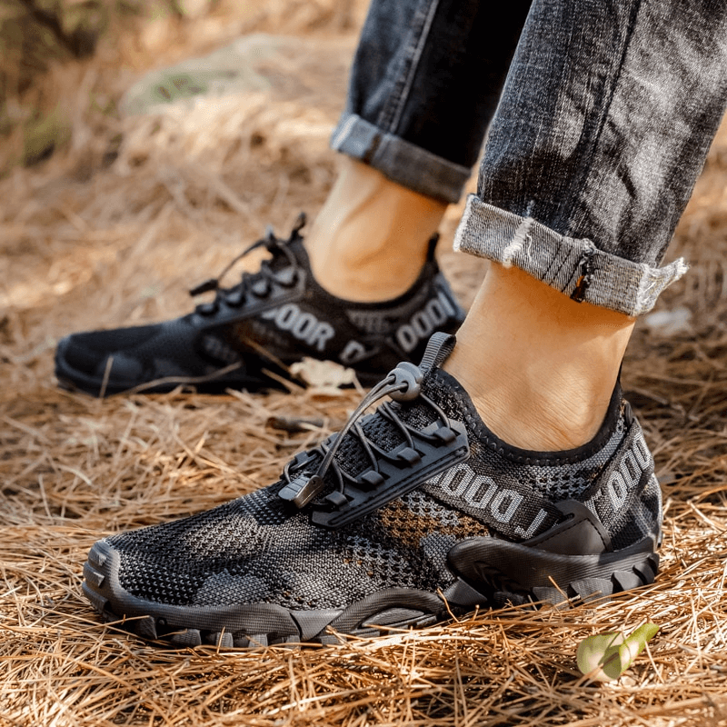 Man wearing soft breathable non-slip trekking sneakers, black, on outdoors pathway.