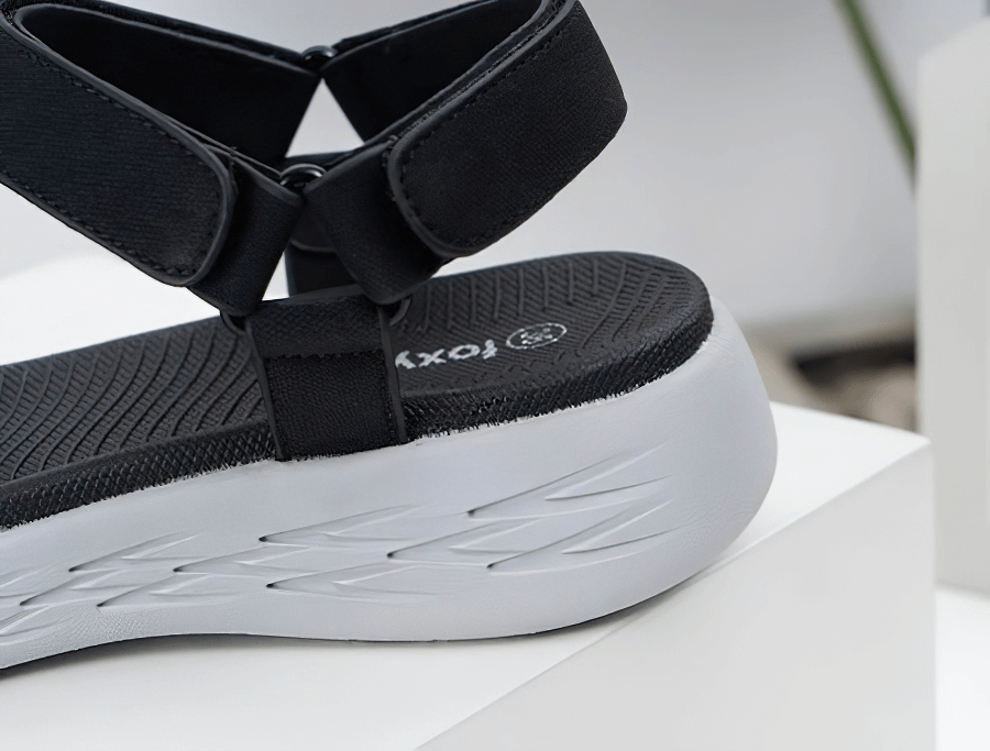 Close-up of a sleek black wedge sandal with a soft sole and sturdy heel, featuring hook & loop closure and a durable rubber outsole.