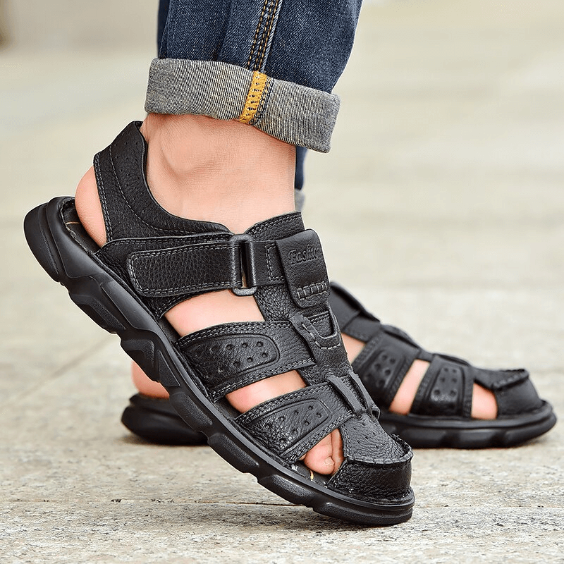 Men's black leather trekking sandals with anti-collision toes worn with jeans, featuring hook & loop closure and rubber outsole for grip.