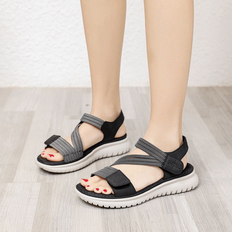 Sport women's soft sandals with Velcro, flat design, black and grey color, on wooden floor, showcasing comfort and style.