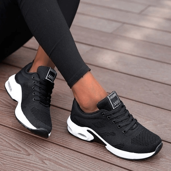 Woman wearing black breathable running shoes with white sole, showcasing flexible, lightweight design on wooden deck.